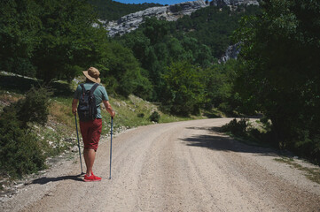 Man Hiking Along a Mountain Path with Walking Sticks and Backpack
