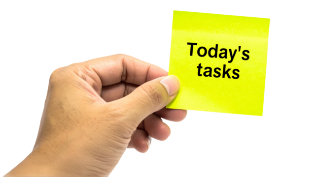 A hand holding a sticky note with "Today's tasks" written on it. Focus is on the task at hand. It's a reminder to be productive
