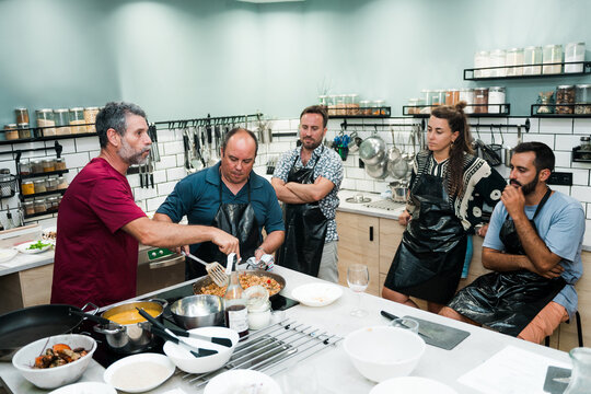 group of young adult friends enjoying a cooking class with a chef, men and women learning to cook - Powered by Adobe