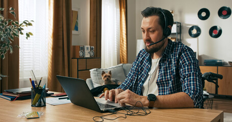 A focused freelancer with a disability sits in a wheelchair, wearing headphones and working online. His role as a remote support operator reflects confidence and digital competence.