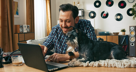 A man with dark hair and a beard speaks to loved ones or teammates during a video call, happily showing his pet dog to the camera while saying goodbye with a smile.