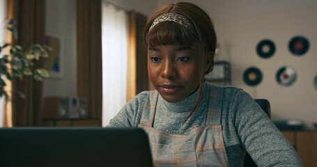 A pretty young girl sits at a home office desk, looking over her calendar and jotting down plans for the week ahead, focused on staying productive and balanced in her work routine.