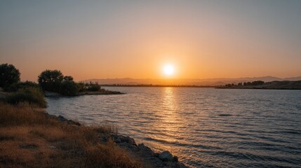 Fototapeta premium Golden hour lake scene reflecting sunlight over water ripples and mountains