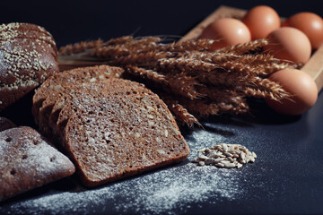 Fresh loaves of bread with wheat and gluten on a black table. Bakery and grocery concept. Fresh, healthy sorts of rye and white loaves food closeup. Fresh homemade bread with cereals.