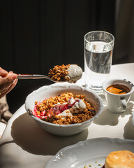 Person eating granola with yogurt and berries for breakfast in sunlight
