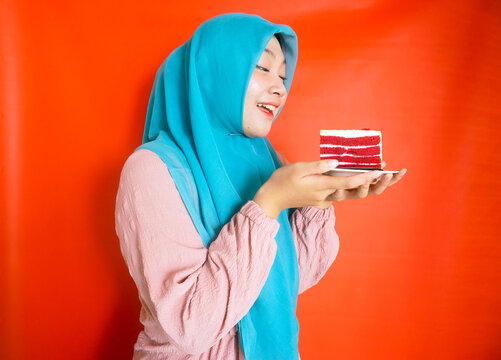 Side View Of Young Girl Holding Red Soft Cake With Happy Expression. Studio Shot