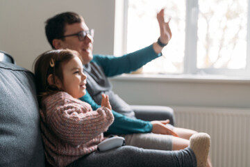 Happy father with child playing wireless console game station. Funny weekend family time at home in living room.