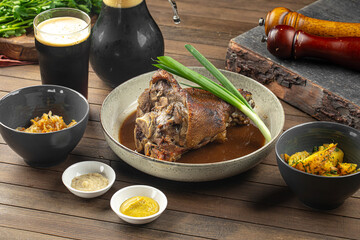 Roasted pork knuckle with sauces cabbage and potatoes on wooden table