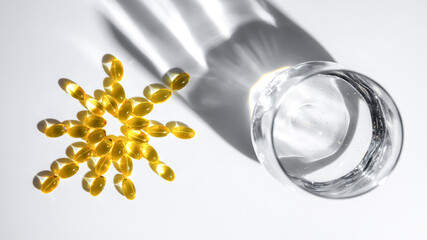 vitamin D or Fish oil yellow transparent capsules forming a sun shape alongside a glass of water...