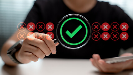 Hand holding magnifying glass with green check mark among red cross symbols. Concept of data...