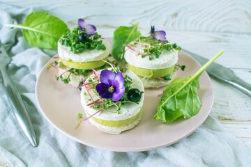 Vegetarian appetizer with cucumber slices, microgreens and feta cheese garnished with fresh purple flowers.