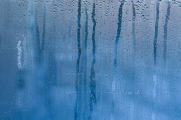 condensation, its translucent blue surface with countless micro-droplets. Some droplets grow heavy to begin their slow descent, leaving trails through fogged surface. abstract wet glass background