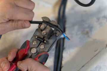 Close-up of electrician's hands using wire strippers to carefully remove insulation from electrical...