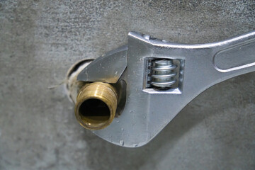 Close-up of a plumber using an adjustable wrench to tighten a brass pipe fitting, ensuring a secure...