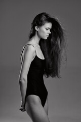Black and white portrait of a slender woman in a black bodysuit with long flowing hair against a...