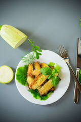 Zucchini with a crispy crust and fresh salad on a gray background