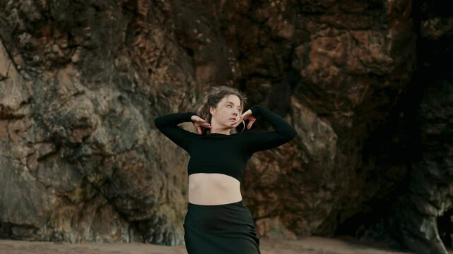 A contemporary dancer elegantly poses in a black outfit, expressing movement and grace against a rocky outdoor backdrop. Captures the essence of freedom and artistic expression.