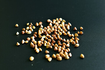 Buckwheat groats are scattered over the surface of a black background.