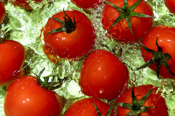 Vegetable background of fresh whole tomatoes in water, splash of water, top view.