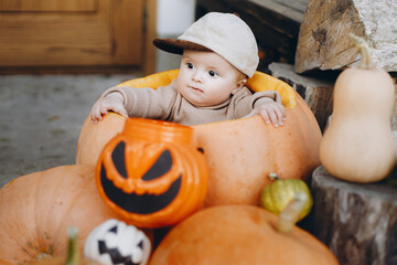 Cute baby boy sitting in big pumpkin with jack o lantern at front door. Happy Halloween and Trick...
