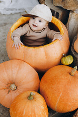 Cute baby boy sitting in big pumpkin at front door. Happy halloween and Thanksgiving. Adorable little child in cozy clothes sitting with pumpkins on porch, autumn decor at home