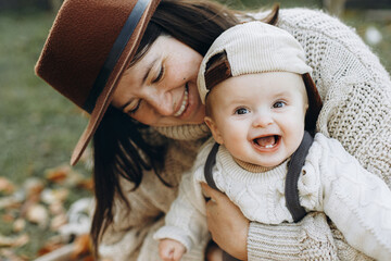 Stylish happy mother and adorable baby son playing on cozy blanket in autumn park. Love and care....