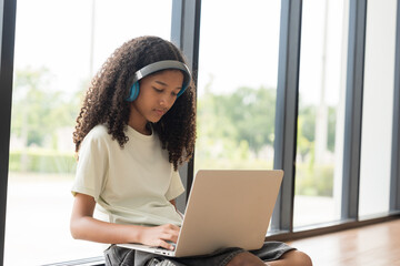 African American male student or kid studying online by using laptop computer and wearing headphone...