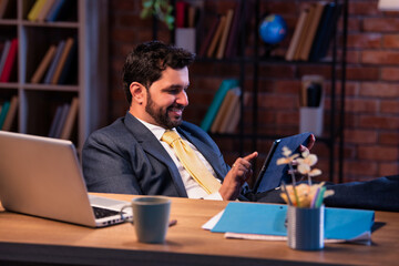 Feet on desk, Indian professional uses tablet, representing relaxed modern business lifestyle