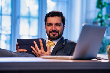 Feet on desk, Indian professional uses tablet, representing relaxed modern business lifestyle