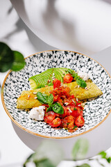 Green omelette with avocado, cherry tomato salsa, goat cheese, basil, and sunflower seeds on a decorative plate.