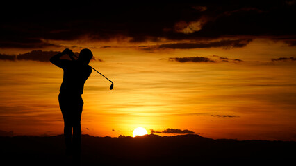 Golfers' hit golf ball toward the hole at sunset silhouetted.