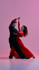 An Argentine tango dance couple strikes a graceful pose against a pink studio backdrop. Concept of...