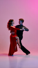 A duo strikes a dynamic Argentine tango stance beneath striking red and purple lighting. An...