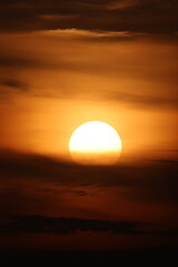 A glowing sun sets behind a layer of dramatic clouds, casting warm golden and amber tones across the sky in The Netherlands
