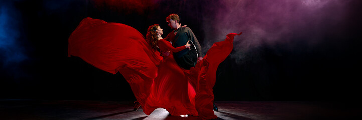 Tango dancers perform with deep passion in a flowing red dress on a softly illuminated stage....