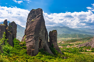 Massive vertical rock formation rising from lush green forest in Meteora Greece