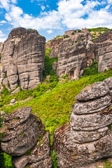 Medieval monastery perched on massive rock formations above lush green valley in Meteora Greece