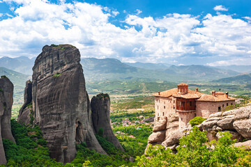 Ancient Meteora monastery perched on cliff edge beside massive rock formation in Greece