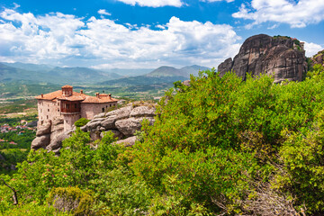 Ancient Meteora monastery perched on cliff edge beside massive rock formation in Greece