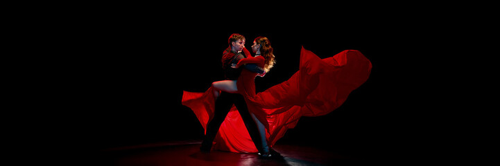 Dramatic dancers of Argentine tango passionately embrace on a dimly lit stage, with a flowing red...