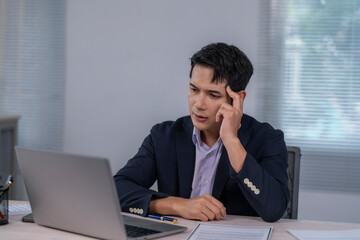 A man in a suit is sitting at a desk with a laptop open in front of him