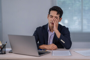 A man is sitting at a desk with a laptop and a stack of papers