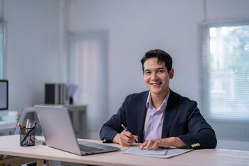 Fototapeta premium A man in a suit is sitting at a desk with a laptop and a pen