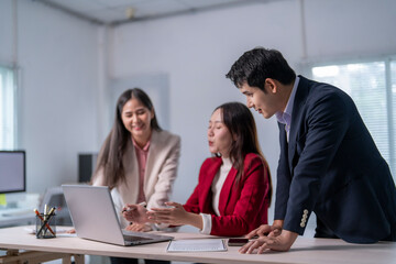 Three people are sitting at a desk with a laptop open