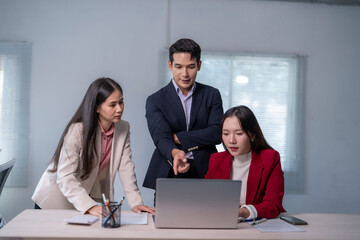 Three people are sitting at a desk with a laptop in front of them