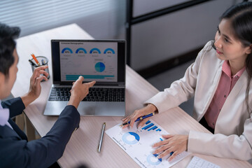 Two people are looking at a laptop screen with graphs on it