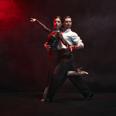 An elegant couple gracefully executes a passionate Argentine tango pose, enveloped in dramatic red...
