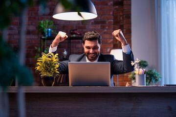 Indian businessman celebrates success at work with laptop, expressing victory and happiness