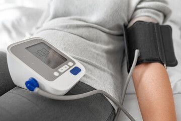 A person checks their blood pressure using a digital monitor while sitting indoors, highlighting a...