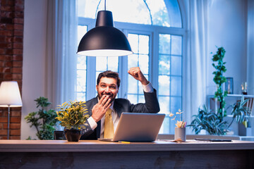 Indian businessman celebrates success at work with laptop, expressing victory and happiness